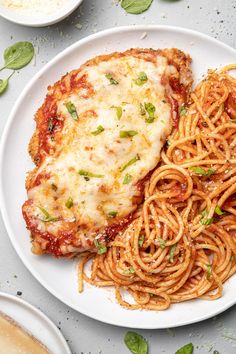 a plate of spaghetti and chicken parmesan on a white plate with basil garnish