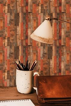 a desk with a notebook, pen holder and lamp next to it on top of a wooden table