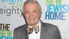 an older man wearing a bow tie standing in front of a new jewish home sign