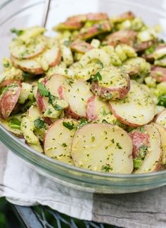 a glass bowl filled with potatoes and broccoli on top of a table cloth