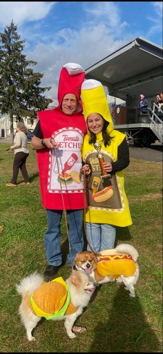 two people in costumes standing next to a dog wearing hot dogs and hamburgers on leashes