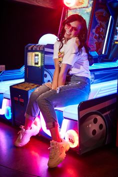 a woman sitting on top of a pinball machine in a room with neon lights