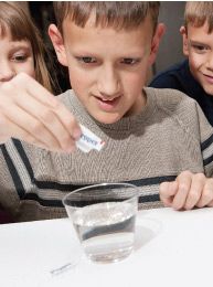 two boys and a girl are looking at something in a small glass on the table