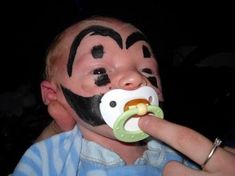 a young child with face painted like a monkey eating a pacifier in his mouth