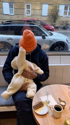 a man sitting at a table with a baby in his lap and an orange hat on