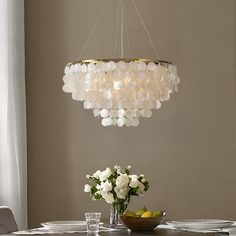 a chandelier hanging over a dining room table with flowers and fruit on it