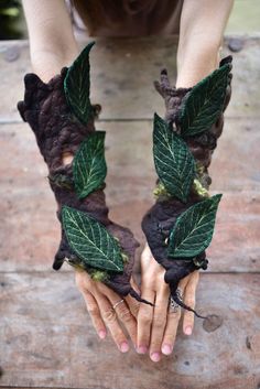 a woman is holding her hands with green leaves on them and wearing gloves made out of felt