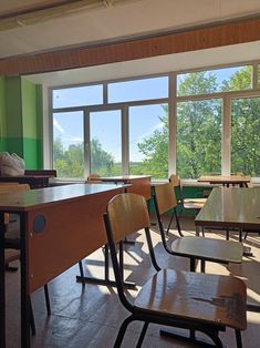 an empty classroom with wooden desks and large windows overlooking the trees in the distance