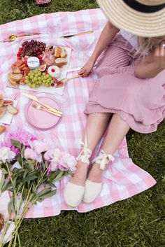 a woman sitting on top of a pink checkered blanket next to food and flowers