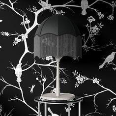 a lamp sitting on top of a table next to a tree wallpapered with birds