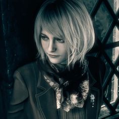 a woman with blonde hair wearing a black jacket and bow tie standing in front of a window