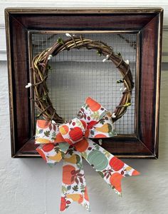 a wreath hanging on the side of a wall next to a frame with a bow