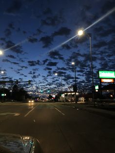 an empty street at night with the lights on and clouds in the sky over it