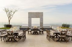 an outdoor dining area overlooking the ocean with tables and chairs set up for a meal