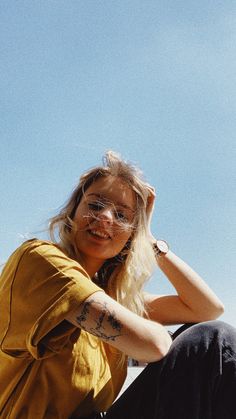 a woman sitting on the ground with her arm around her head, wearing glasses and a yellow shirt