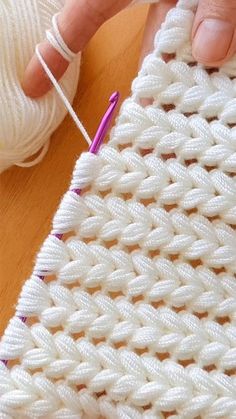 someone is knitting on a white piece of yarn with a purple crochet hook