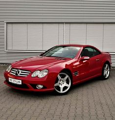 a red mercedes slk parked in front of a building