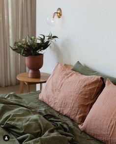 a bed with green sheets and two pink pillows on top of it next to a potted plant