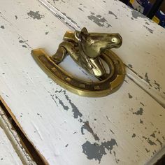 a brass frog door knocker sitting on top of a white painted wooden table with peeling paint