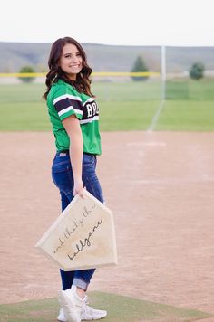 a woman holding a sign on top of a baseball field while wearing a green shirt