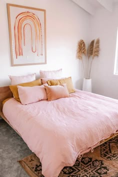 a bed with pink comforter and pillows in a white room next to a window