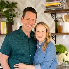 a man and woman standing in front of a kitchen counter with flowers on the shelves