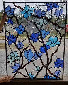 a person is holding up a stained glass window with blue flowers and branches on it