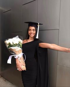 a woman in a graduation cap and gown holding flowers, with her arms outstretched out