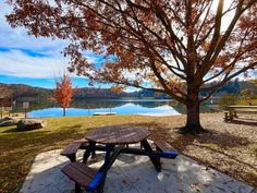 a picnic table sitting in front of a tree next to a lake with autumn leaves on it