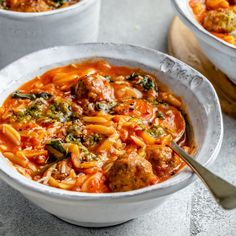 two white bowls filled with pasta and meat soup on top of a table next to a wooden spoon