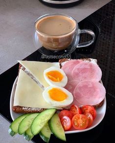 a plate with eggs, ham, tomatoes and cucumbers on it next to a cup of coffee