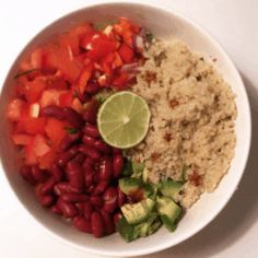 a white bowl filled with rice, beans and veggies next to a lime