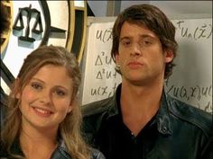 a man and woman standing next to each other in front of a wall with writing on it