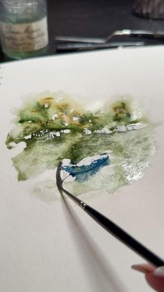 a person is holding a paintbrush and drawing on paper with watercolors in front of them