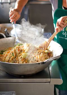 a person cooking food in a wok on top of a stove with a wooden spoon