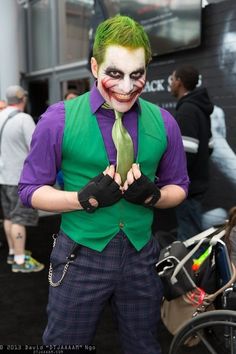 a man dressed up as the joker with green hair and purple shirt holding a tie