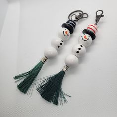 two snowmen wearing hats and tassels are on the same keychain