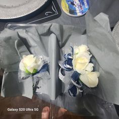 two white roses are sitting on the table next to silver plates and napkins that have been wrapped in clear cellophane