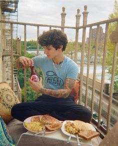 a person sitting on a balcony with food and drinks in front of him, while holding a bottle of beer