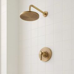 an overhead shower head and thermostaer in a white tiled bathroom with gold faucet