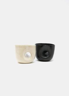 two black and white bowls sitting next to each other on a white surface with an oval hole in the middle