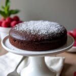 a chocolate cake with powdered sugar on top sitting on a white plate next to strawberries