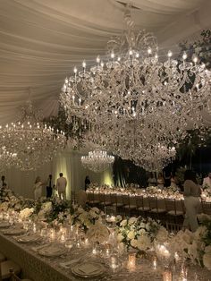 a large chandelier hanging from the ceiling in a banquet hall filled with white flowers and candles