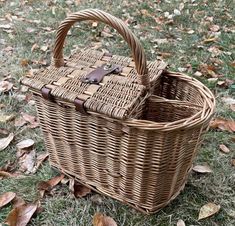 a wicker picnic basket sitting in the grass with leaves on the ground next to it