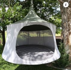 a white tent hanging from a tree in the grass with trees around it and green grass on the ground