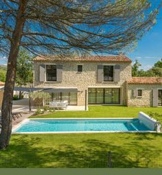 an outdoor swimming pool in front of a large house with trees and grass around it