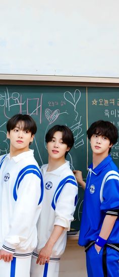 three boys standing in front of a blackboard with writing on it and one boy wearing blue