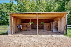 the inside of a horse barn with two stalls and horses in the back ground, surrounded by trees