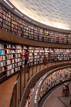 the inside of a library with many bookshelves and people standing on them in it