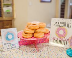 a table topped with lots of donuts on top of a pink cake stand next to greeting cards